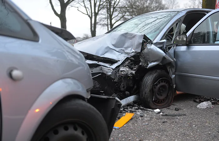 Two silver cars after a severe head-on collision, showing major damage and debris on the street.