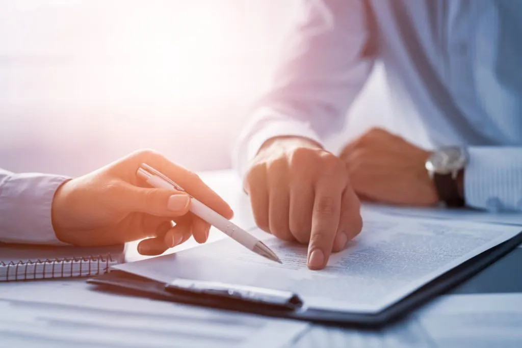 Two professionals are reviewing a document on a desk.