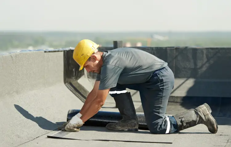 A man in a hard hat and work boots is positioned on a roof