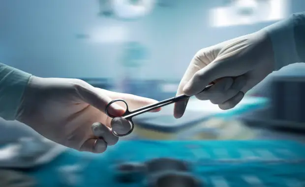 A close-up of two hands holding surgical scissors in an operating room environment.