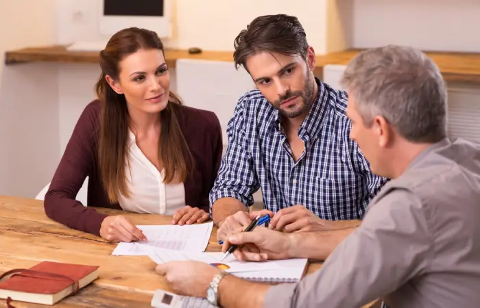 A group of three people at a table, engaged in conversation while examining documents.