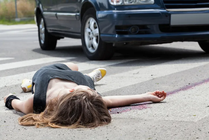 A young woman lying face-up on a pedestrian crossing after being hit by a car.