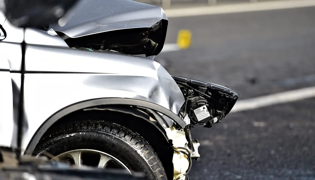 A damage bumper and headlight of a silver car.