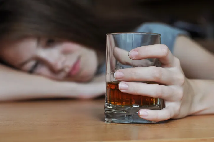 A woman holding a glass tumbler half-filled with liquor.