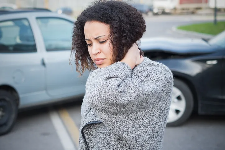 A woman clutching her neck and shoulder with a painful expression.