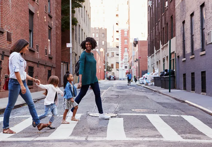 The adults are holding the children's hands, and the woman in the green sweater is smiling as they walk in pedestrian.