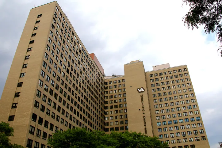 VA Medical Center building is shown from a low-angle perspective against an overcast sky.