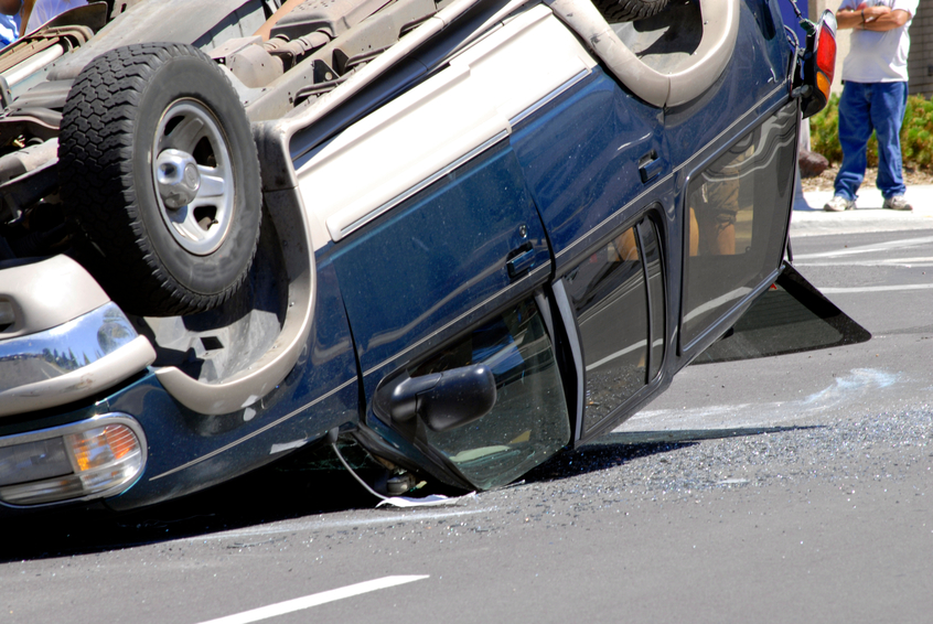 An overturned car lying upside down on the street, with its wheels in the air and debris scattered around.
