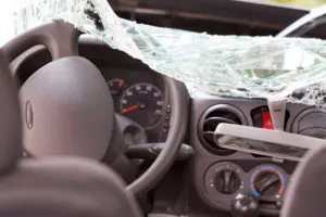 An image of a car's interior after an accident, showing a shattered windshield, the steering wheel, and the dashboard.