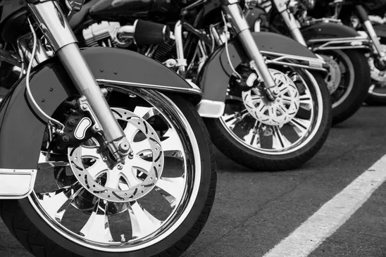 The front wheels and fenders of a row of chrome-heavy cruiser motorcycles parked on the road.
