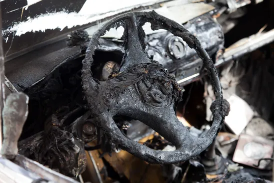 A burnt, melted, and charred steering wheel and dashboard of a wrecked vehicle.
