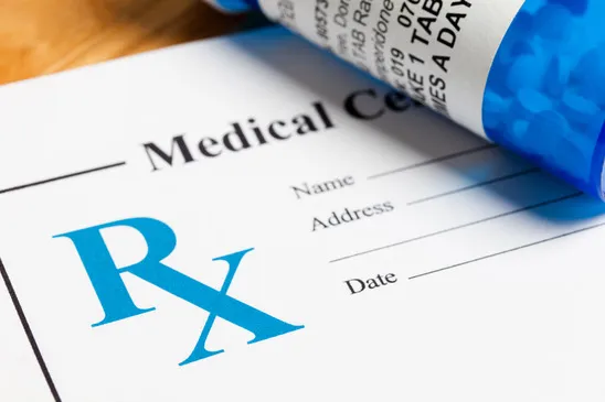 A prescription pad with the blue 'Rx' symbol next to a blue pill bottle.