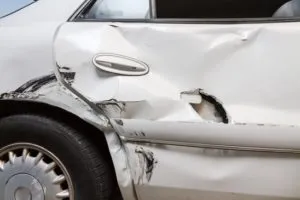 A white car's rear passenger door and fender, severe damage and crumpled dent and a hole.