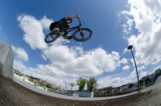 BMX rider doing a mid-air jump over a skatepark against a bright blue sky.