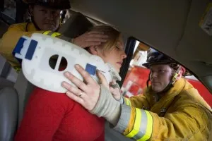 Firefighters securing a neck brace onto an injured woman in a car.