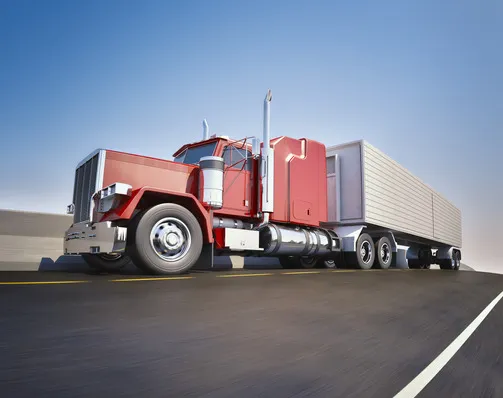 Red semi-truck hauling a white refrigerated trailer on a highway under a clear blue sky.