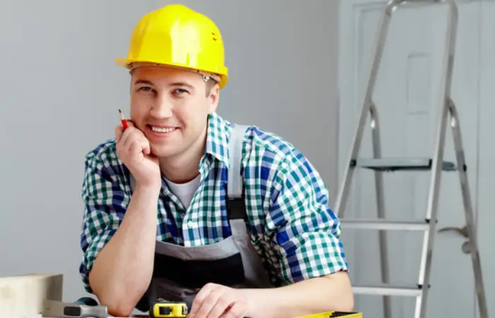 A man in a hard hat examines a construction plan while seated at a table, indicating a work environment