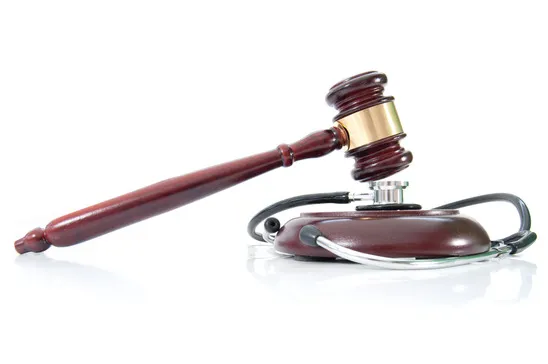 Wooden gavel resting on a stethoscope against a white background, symbolizing medical law or legal issues in healthcare.