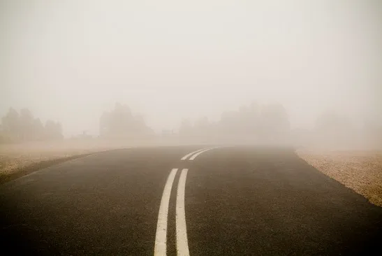 A double white center lines curving slightly to the right while dominated by heavy thick fog.