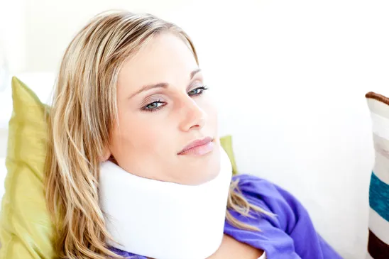 A blonde woman wearing a white neck brace is lying on a sofa