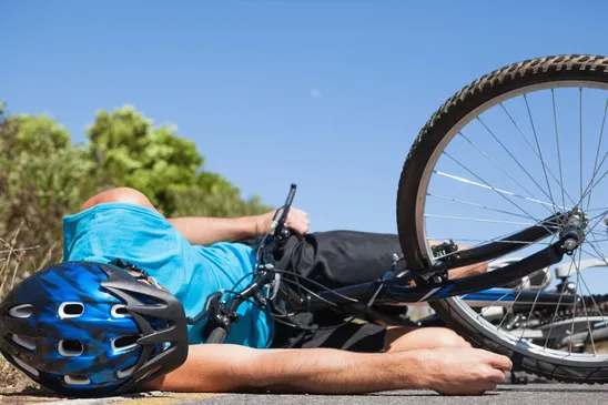 A cyclist wearing a blue shirt s lying on his side on the pavement next to his bicycle after an accident.