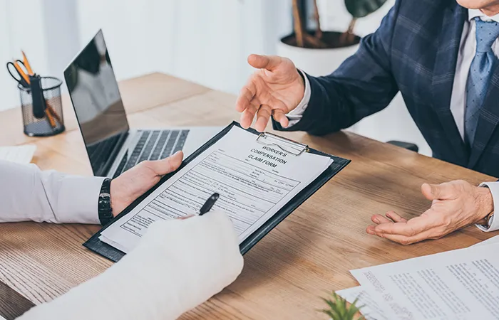 Two people in formal wear at a desk, signing a Worker's Compensation Claim Form.