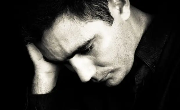 A man sits with his head in his hands, expressing distress or frustration.