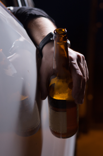 Drunk young man driving a car with a bottle of beer. Don't drink and drive concept.