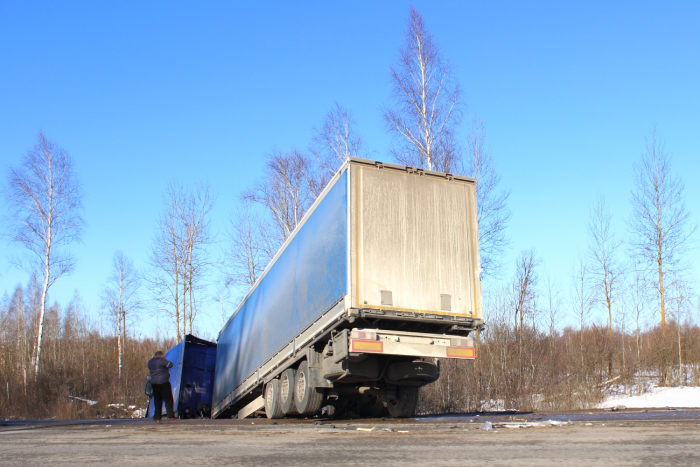 Tilted semi truck in roadside ditch – vehicle crash, skid, black ice, road accident on day winter road on trees and blue clear sky background.