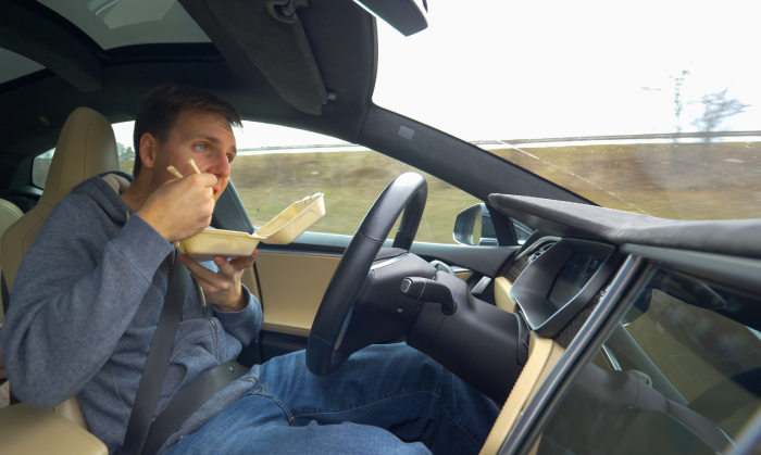 Reckless young man eating Chinese take out food with chopsticks while driving in his high tech car. Male driver eating while driving back home from work. Man driving in autonomous vehicle