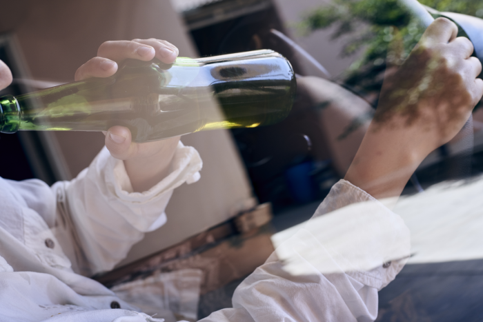 A woman driving a car while drinking beer from a bottle as seen through a car glass window. Drunk diving, unsafe driving concept