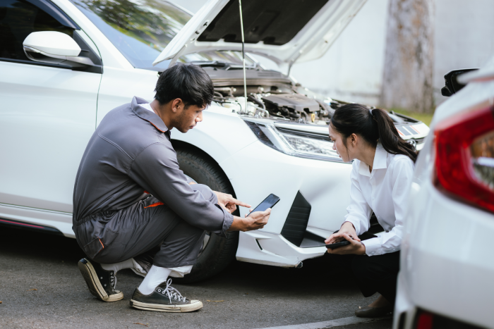 Insurance agent holding clipboard talking to car accident victim, inspecting damaged car parked on road after crash to analyze claim.
