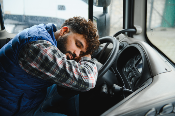 Truck driver resting head on steering wheel, exhausted and drowsy after long haul, taking a break in the parked cabin